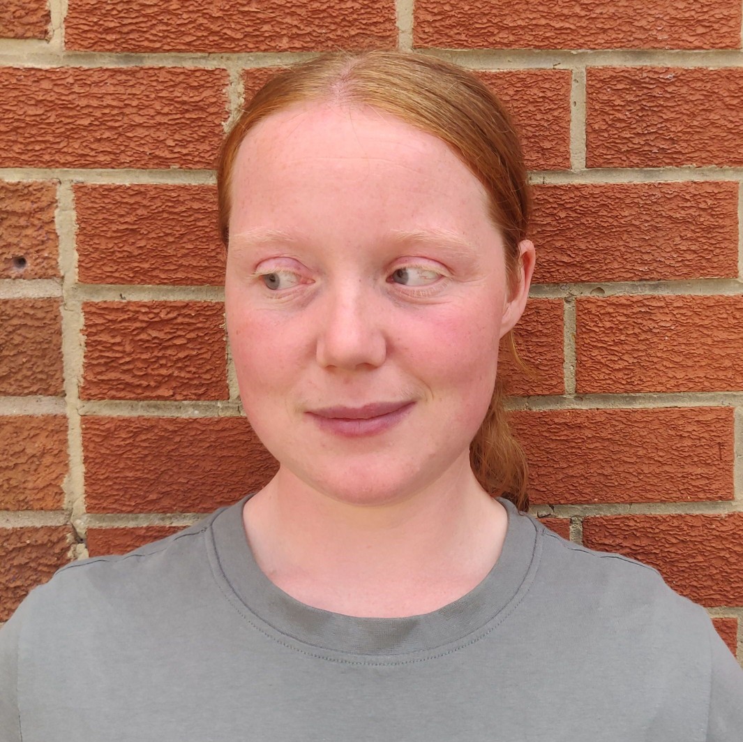 Photograph of Hollie, head and shoulders, against a red brick wall